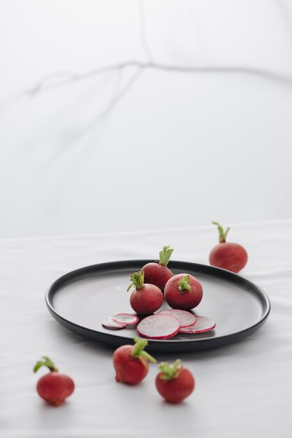 Fresh red radishes with stem and roots in a black dish on table