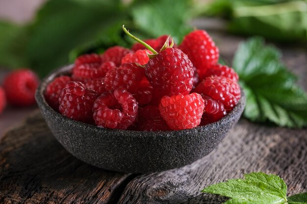 Fresh red raspberries in bowl on wooden dark table. Closeup berries background.