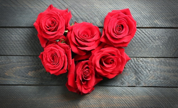 Fresh red roses buds in shape of heart on wooden background