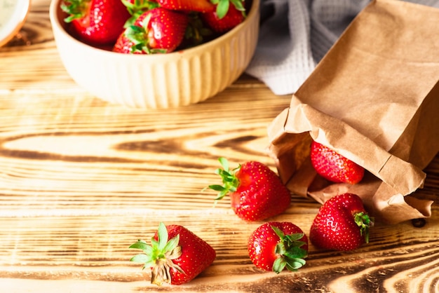 Fresh red strawberries in the bowl and paper bag in the wooden background Rustic style