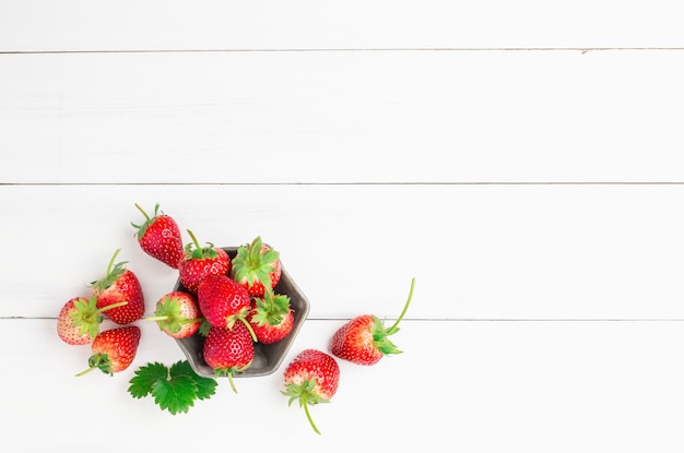 Foto fragole rosse fresche in una tazza di ceramica della ciotola sul pavimento di legno bianco della plancia per fondo.