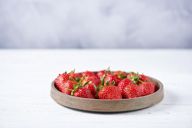 Photo fresh red strawberries in a grey ceramic plate on a white wooden table close up copy space