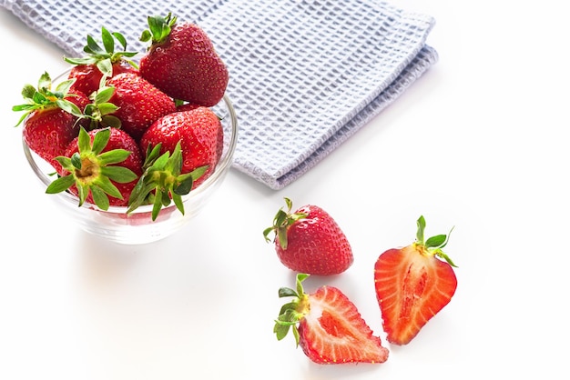 Fresh red strawberries in transparent bowl and small kitchen towel isolated on white background