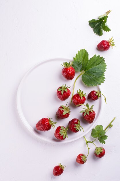 Fresh red strawberry in a bowl with green leaf on white surface. Top view