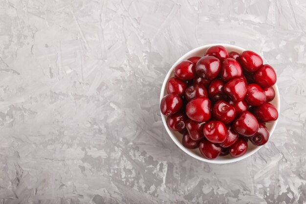 Fresh red sweet cherry in white bowl on gray concrete copyspace. top view