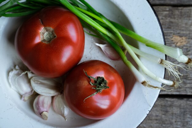 Fresh red tomatoes, garlic, and scallions on old wooden table closeup view