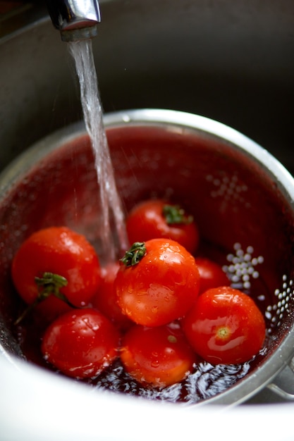 Fresh red tomatoes splashing in water before cooking at home, washes in a metal sink in the kitchen, hygiene.