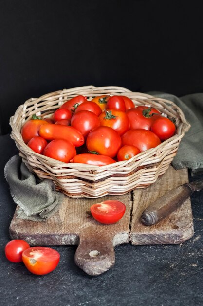 Fresh red tomatoes in whicker basket on black background.