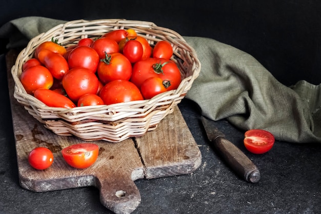 Fresh red tomatoes in whicker basket on black background.