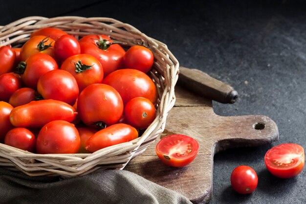 Fresh red tomatoes in whicker basket on black background.