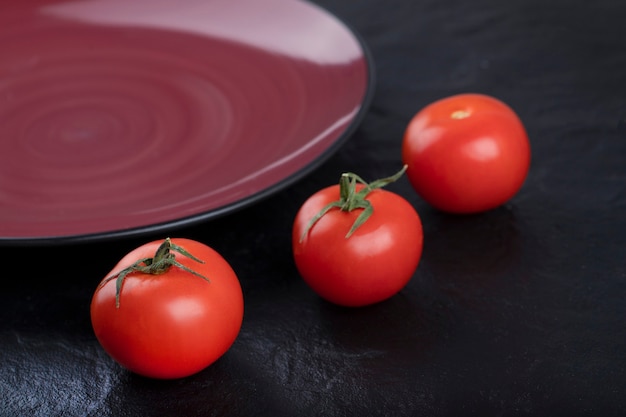 Fresh red tomatoes with plate placed on black table . 