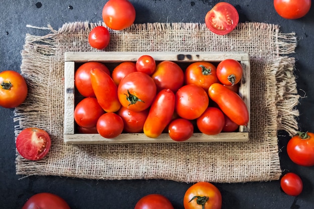 Fresh red tomatoes in wooden box on black background. Flat lay, top view