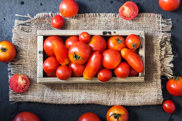 Pomodori rossi freschi in scatola di legno su sfondo nero. disposizione piatta, vista dall'alto