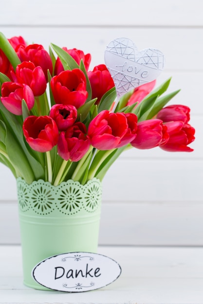 Fresh red tulip flowers bouquet on shelf in front of wooden wall.