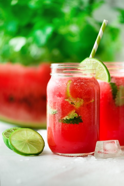 Fresh red watermelon smoothie in glass jar with straw, ice, mint and lime 