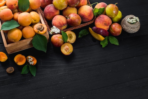 Fresh ripe apricots and plums on black wooden background. Copy space