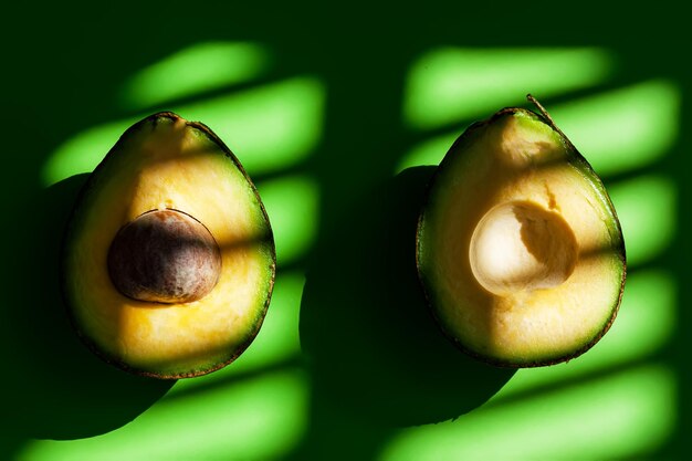 Foto avocado maturo fresco tagliato a metà sullo sfondo verde con ombre di luce solare naturale