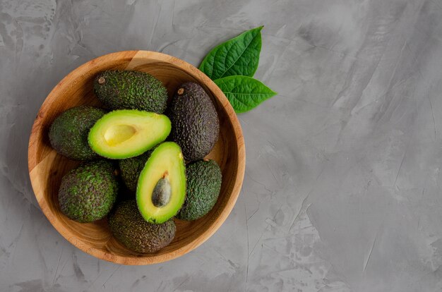 Avocado maturo fresco con foglie in un piatto di legno