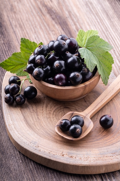 Fresh ripe black currant in wooden bowl with original leaves on rustic old background