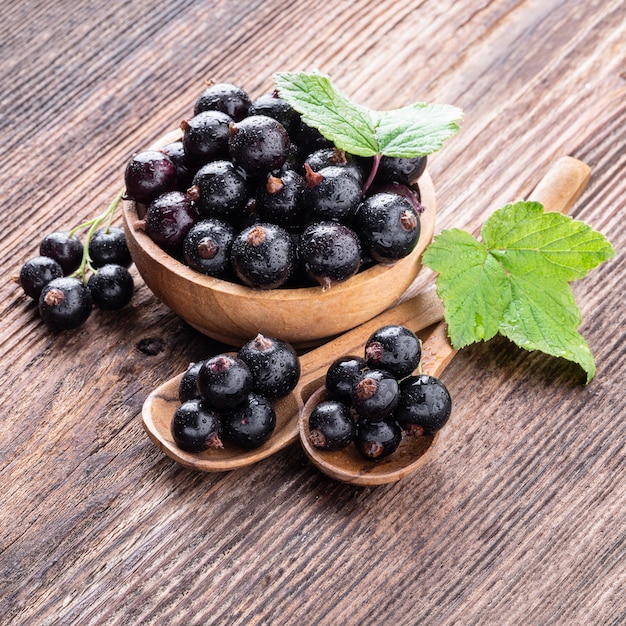 Fresh ripe black currant in wooden bowl with original leaves and two spoons