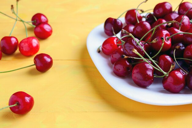 Fresh ripe cherries in a bowl with water drops on yellow wooden background