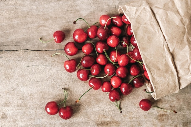 Fresh ripe cherries in a paper bag on wooden background Top view Copy empty space for text