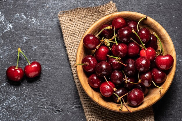 Fresh ripe cherries in wooden bowl on black rustic background top view.