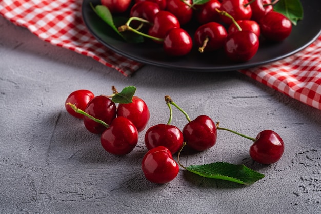 Fresh ripe cherry fruits with green leaves on black plate