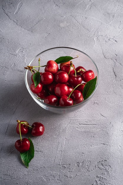 Fresh ripe cherry fruits with green leaves in glass bowl