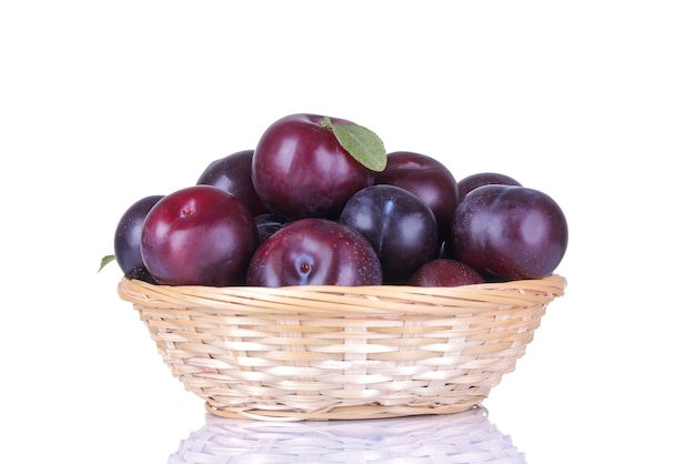 Fresh ripe delicious plums in a wicker basket on a white isolated background