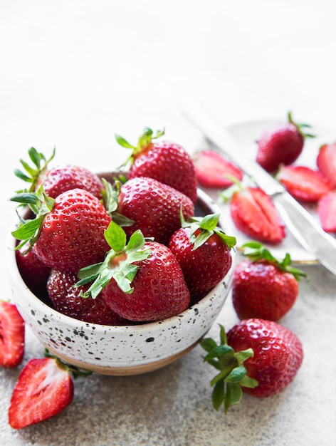 Fresh ripe delicious strawberries in a white bowl on a gray stone background