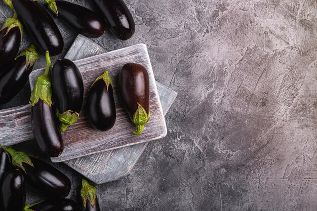 Fresh ripe eggplant on wooden cutting board, stone concrete table, top view copy space
