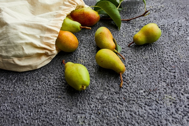 Pere fresche di frutta matura in una borsa ecologica riutilizzabile per la spesa su uno sfondo scuro, concetto di drogheria, piatto, ecologico, raccolto autunnale. copia spazio.