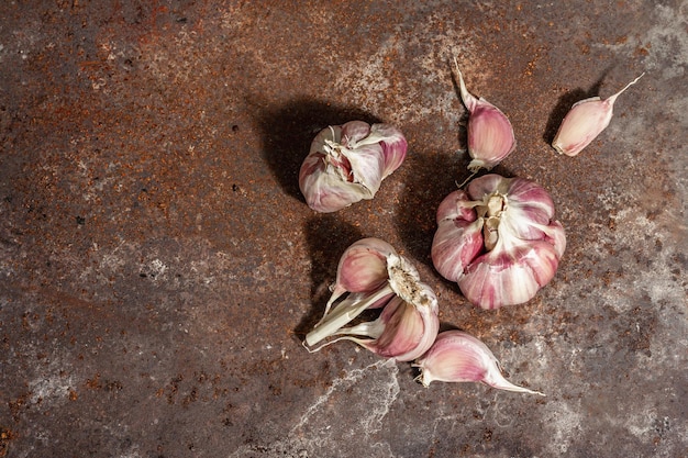 Fresh ripe garlic cloves on a rusty metal background, close up. Trendy hard light, dark shadow, flat lay, top view