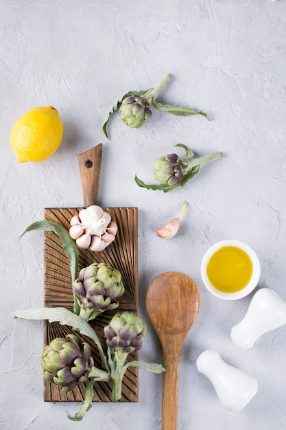 Fresh ripe green artichokes on cutting board ready to cook and ingredients garlic, lemon and olive oil