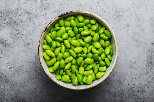 Fresh ripe green edamame beans without pods in bowl on gray stone background. Top view, close up. Light and healthy asian snack good source of vegetarian protein for diet and nutrition