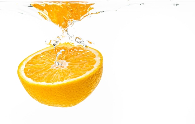 Fresh ripe half of orange fruit sinking in the clear water isolated on white background