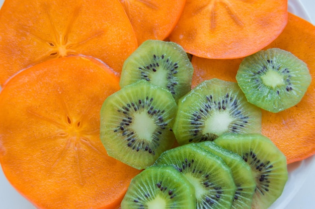 Fresh ripe juicy kiwi slices with persimmon arranged on a plate top view