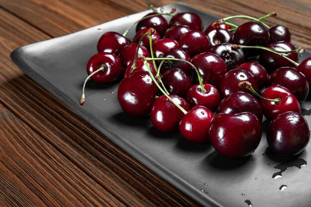 Fresh ripe juicy sweet cherries in a black plate on a wooden background Wet fresh cherries