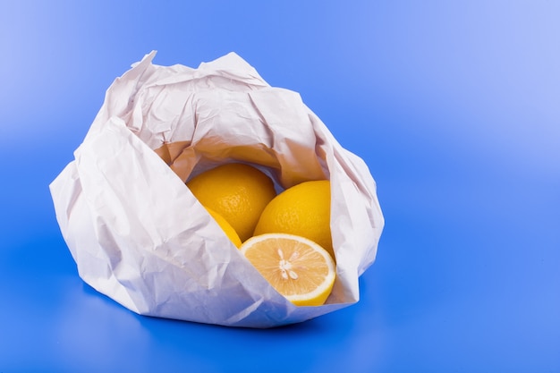 Fresh ripe lemons in paper bag on blue background