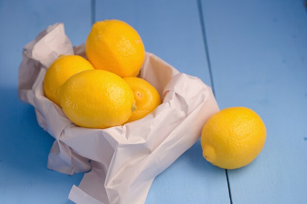 Fresh ripe lemons in paper bag on blue table background