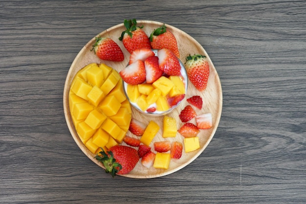 Fresh ripe mango and strawberry fruit in a cup with cookies soy yogurt on a wooden plate