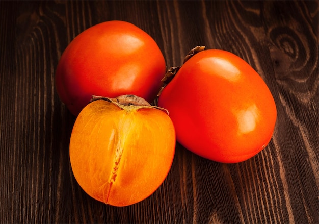 Fresh ripe orange persimmon and slice on a wooden background