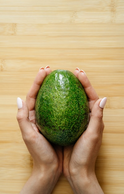 Photo fresh ripe organic green avocado in female hands on woden table