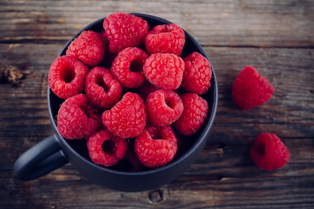 Fresh ripe organic raspberries in a mug on a wooden background