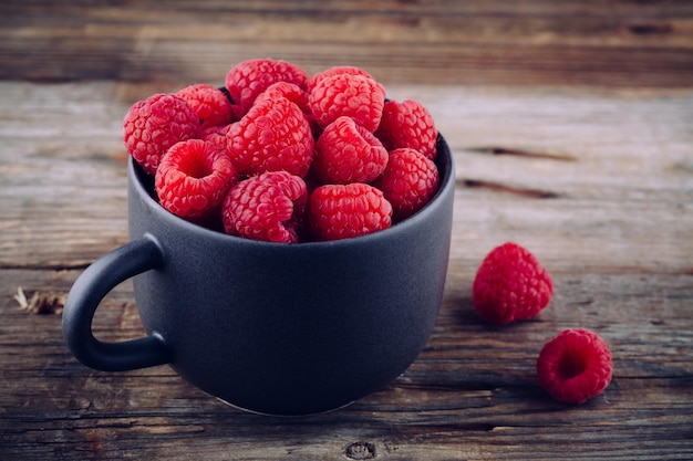 Fresh ripe organic raspberries in a mug on a wooden background