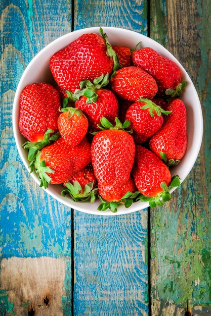 Fresh ripe organic strawberries in a white bowl top view on a rustic wooden table