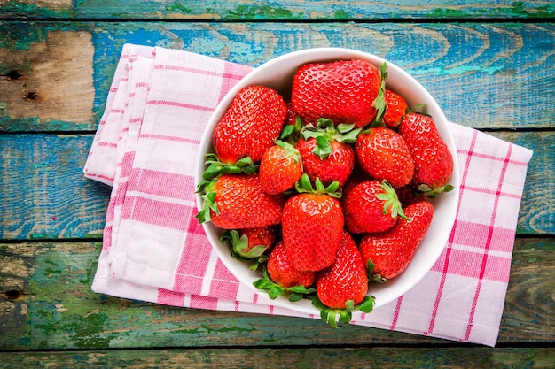 Fresh ripe organic strawberries in a white bowl top view on a rustic wooden table