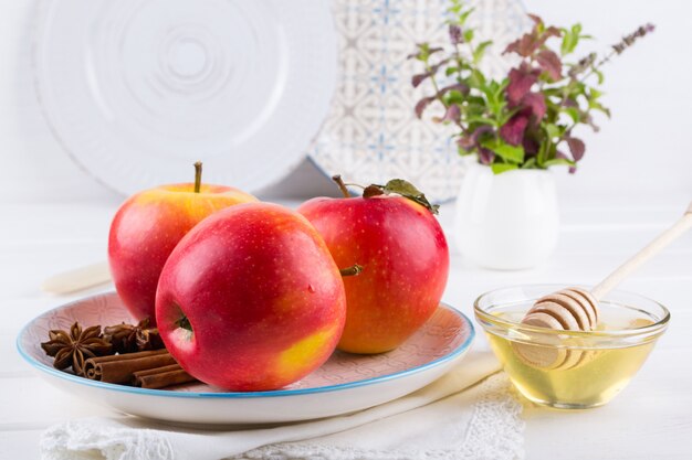 Fresh, ripe organic sweet apples in dish with cinnamon sticks, anise stars and honey on a white kitchen table