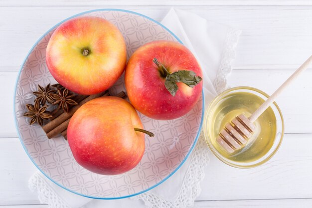 シナモンスティック、アニススター、白いキッチンテーブルの上の蜂蜜が付いている皿に新鮮で熟した有機甘いリンゴ。